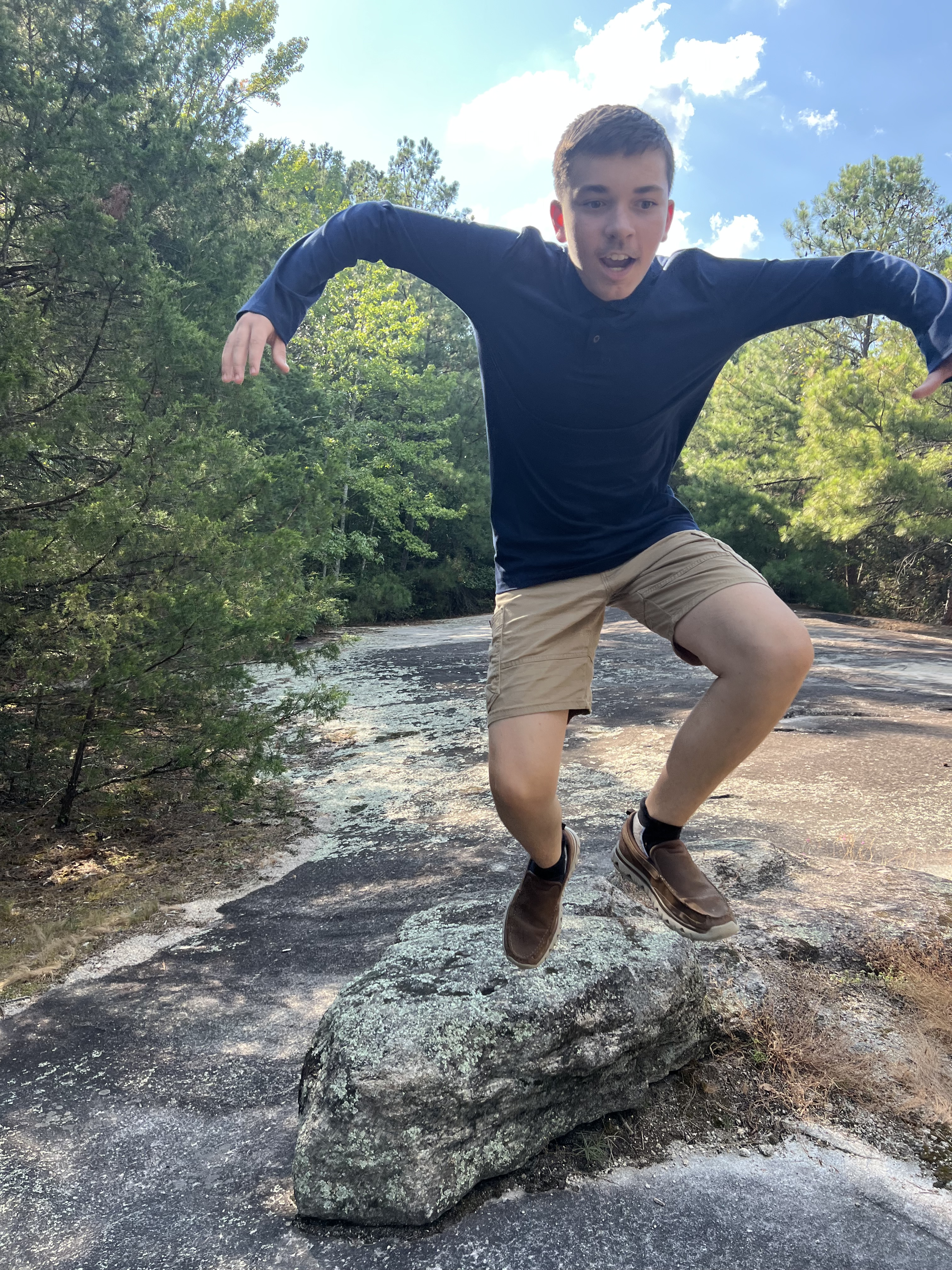 Kingston jumping off a rock in the woods with trees in the background
