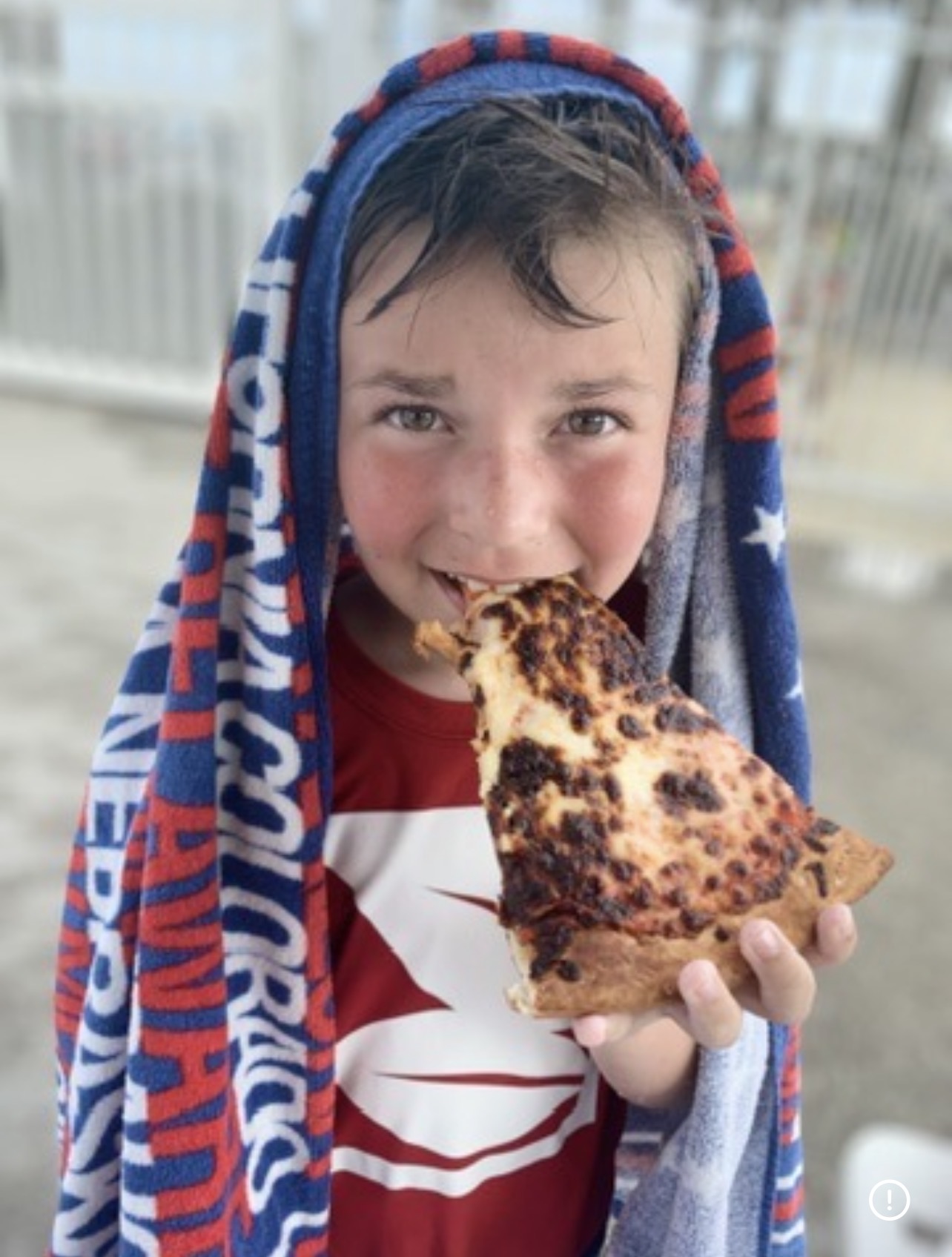 Young Kingston at the beach wrapped in a towel and eating pizza