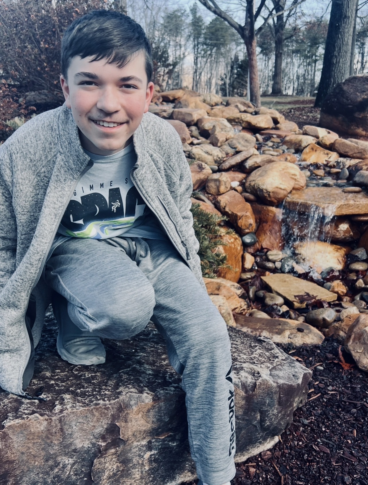 Kingston sitting on rocks beside a small waterfall and smiling