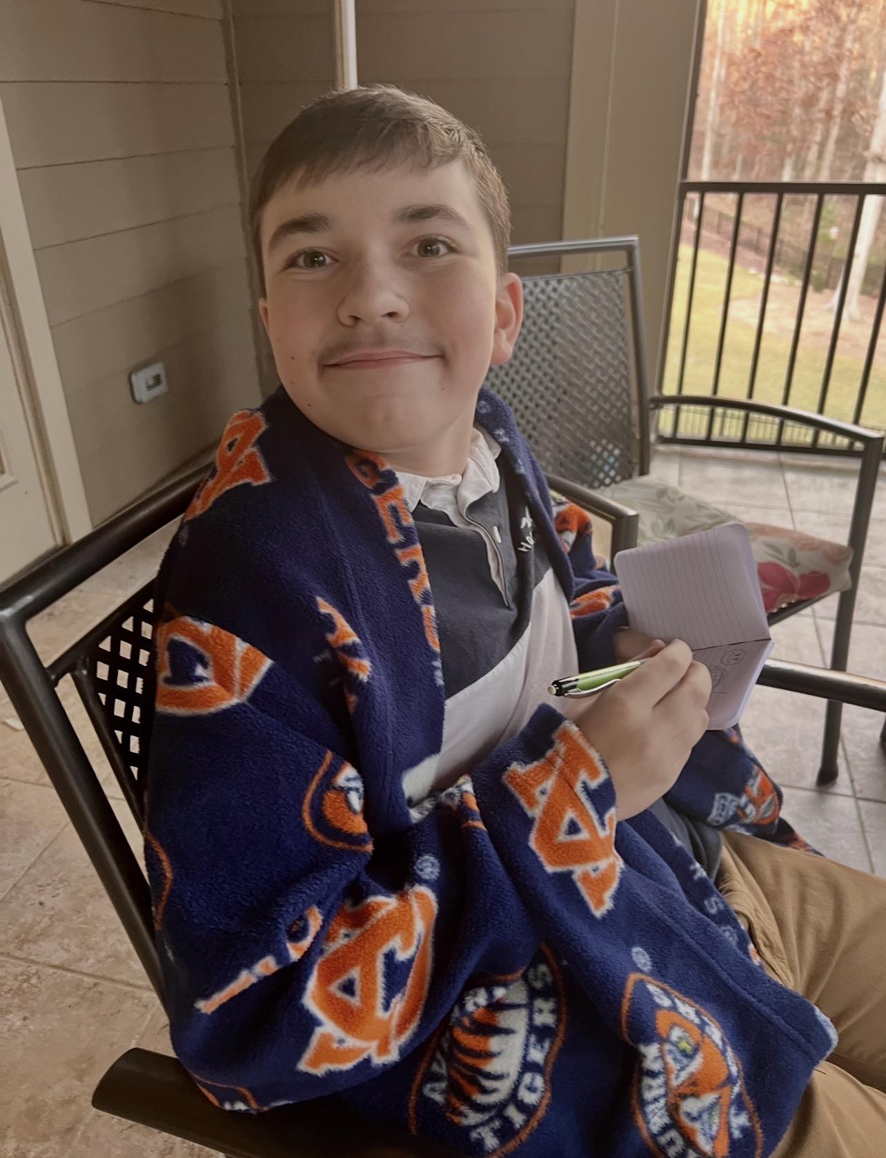 Kingston wrapped in an Auburn blanket on a porch while writing in a notebook
