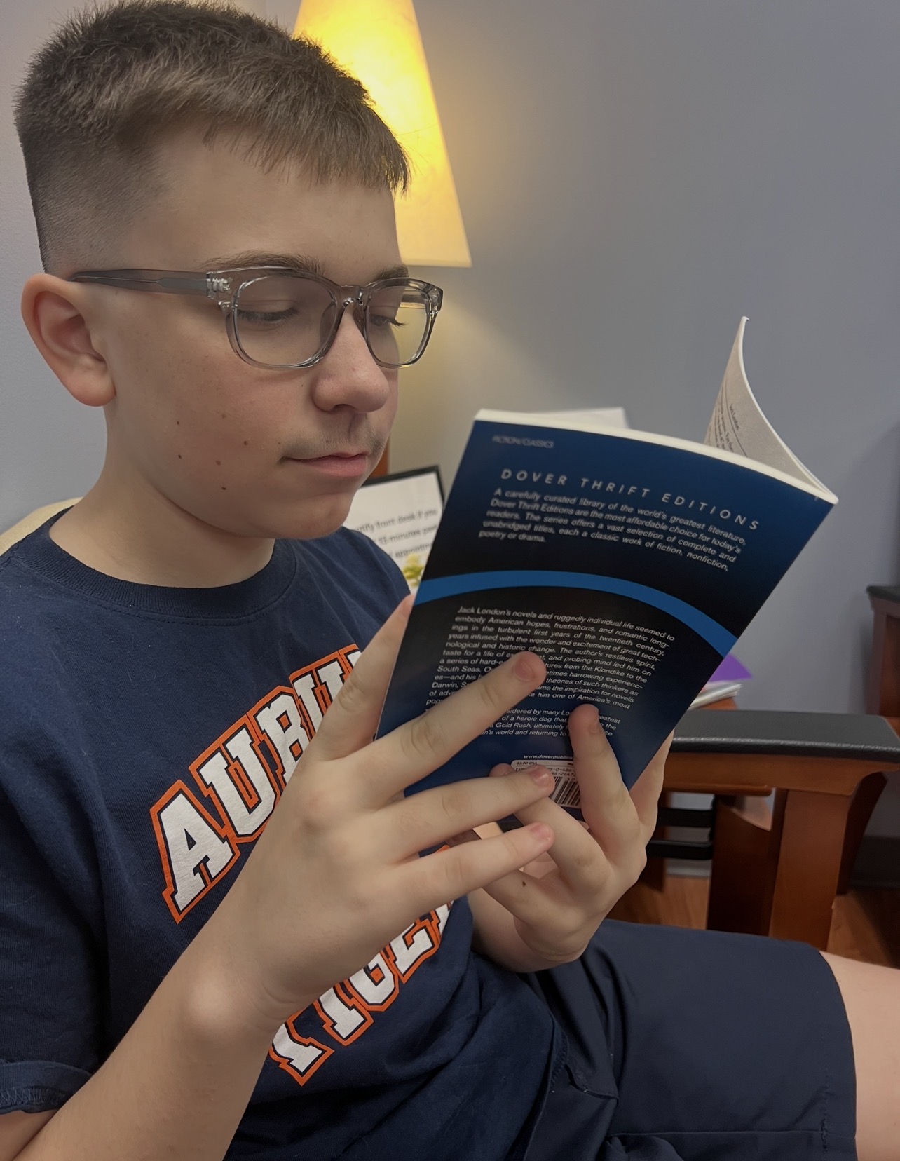 Kingston wearing an Auburn shirt and glasses while reading a book